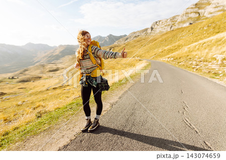 Woman with backpack walking along road with outstretched hand catching car with mountain landscape. Woman with backpack walking along road with outstretched hand catching car with mountain landscape. 143074659