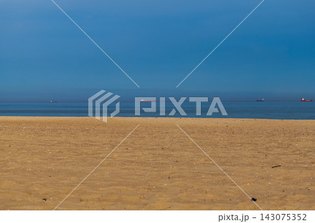 Sandy beach and distant cargo ships on Baltic Sea shore at midday 143075352