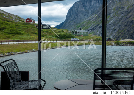 Interior view through large windows overlooking fjord valley with red cabin, Norway Interior view through large windows overlooking fjord valley with red cabin, Norway 143075360