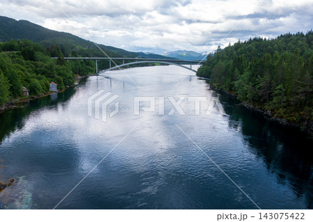 Aerial view of river valley with modern arch bridge and coniferous forest, Norway 143075422