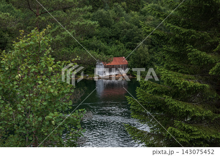 Boathouse with red metal roof on forested waterway, Norway Boathouse with red metal roof on forested waterway, Norway 143075452