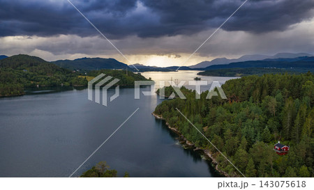 Aerial view of Straumen lake with coniferous forest, mountains and red cabin, Norway 143075618