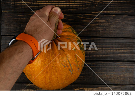 Hand holding a pumpkin on a wooden table during autumn season Hand holding a pumpkin on a wooden table during autumn season 143075862