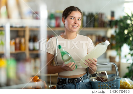 Girl hold packages bottles and choose consider soda water in store Girl hold packages bottles and choose consider soda water in store 143078496
