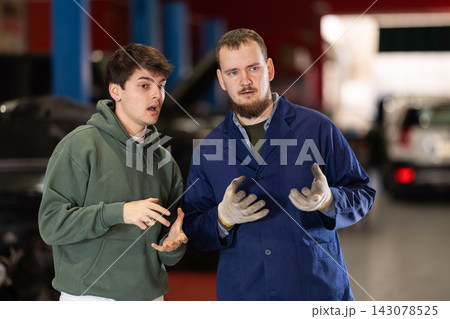 Guy discusses further repairs to his car with car mechanic at car service center Guy discusses further repairs to his car with car mechanic at car service center 143078525