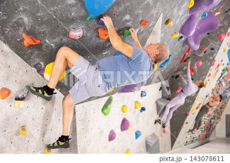 Concentrated elderly man moving on bouldering wall in climbing gym 143078611