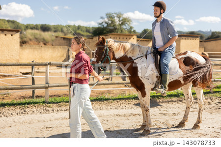 Young woman leading horse with man riding 143078733