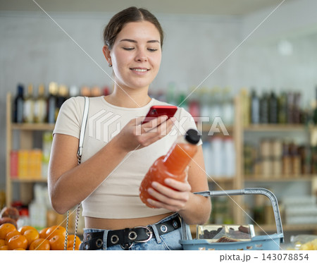 European young woman customer at shop scans QR code on grapefruit juice bottle using phone camera European young woman customer at shop scans QR code on grapefruit juice bottle using phone camera 143078854