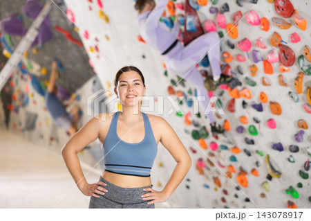 Smiling sporty girl posing near climbing wall at bouldering gym 143078917