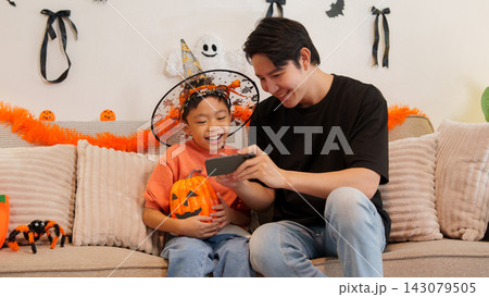 Asian father and son looking at smartphone together during Halloween celebration Asian father and son looking at smartphone together during Halloween celebration 143079505