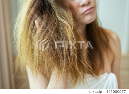 Cropped shot view of young Asian woman holding her damaged split ended hair. Hair damage is risk for further damage and breakage. It may also look dull or frizzy and be difficult to manage. Cropped shot view of young Asian woman holding her damaged split ended hair. Hair damage is risk for further damage and breakage. It may also look dull or frizzy and be difficult to manage. 143080077