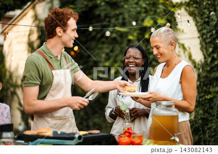Man serving burgers to friends at outdoor BBQ party Man serving burgers to friends at outdoor BBQ party 143082143