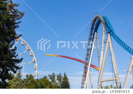 Roller coaster and Ferris wheel attractions in amusement park under blue sky 143085015
