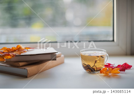 Cozy autumn still life with hot tea, books and fall leaves by rainy window 143085114