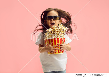 Cheerful Little Girl in 3D Glasses and Holding Popcorn Bucket Watch a Thrill Cartoon Movie Jumping with Popcorn that Flying to Asides Standing on Soft Pink Isolated. Movie Premiere. Cheerful Little Girl in 3D Glasses and Holding Popcorn Bucket Watch a Thrill Cartoon Movie Jumping with Popcorn that Flying to Asides Standing on Soft Pink Isolated. Movie Premiere. 143086832