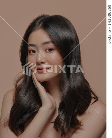 Beautiful brunette asian woman with a clean healthy skin touching her face over beige background, vertical close up shot. 143086869