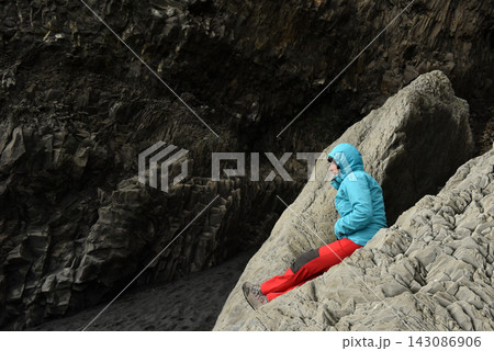 Hiker resting on smooth volcanic rock formations near Halsanefshellir cave Iceland Hiker resting on smooth volcanic rock formations near Halsanefshellir cave Iceland 143086906