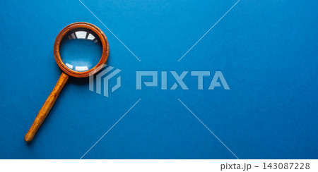 Vintage wooden magnifying glass with brass ring on vibrant blue background 143087228