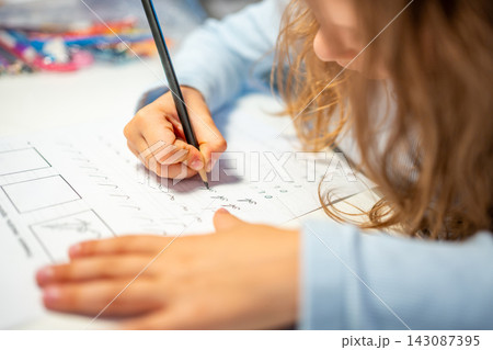 First grade girl practices handwriting with pencil in school workbook. Child learns to write letters during early education with selective focus and shallow depth of field 143087395