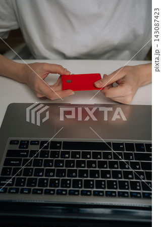 Vertical cropped shot of person holding red credit card while using laptop computer, representing online shopping, financial transactions, secure electronic payment through e-commerce platforms. Vertical cropped shot of person holding red credit card while using laptop computer, representing online shopping, financial transactions, secure electronic payment through e-commerce platforms. 143087423