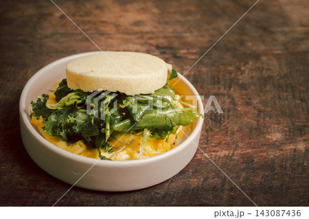 Breakfast muffin sandwich with scrambled eggs and kale in a ceramic place on wooden table. Breakfast muffin sandwich with scrambled eggs and kale in a ceramic place on wooden table. 143087436