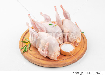 Raw Quail Carcasses as Natural Protein Food on a round wooden serving board with rosemary sprigs and a small bowl of salt, isolated food preparation still life 143087620