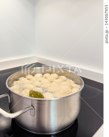 Pot of meat dumplings boiling with a bay leaf on a black induction hob Pot of meat dumplings boiling with a bay leaf on a black induction hob 143087955