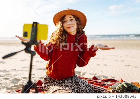 Style woman using smartphone with stabilizer, taking pictures in on sea beach. Woman creates content 143088043