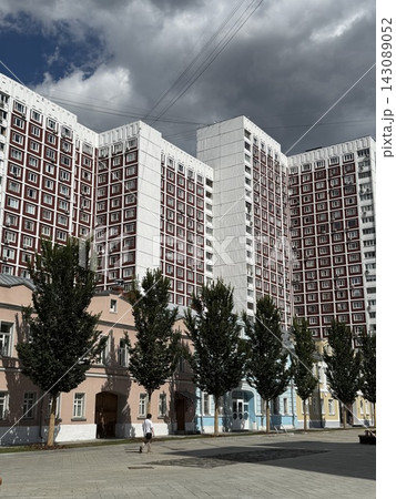 Urban apartment buildings with colorful facades, trees, overhead wires, and dramatic cloudy sky Urban apartment buildings with colorful facades, trees, overhead wires, and dramatic cloudy sky 143089052