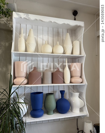 Colorful ceramic vases arranged on a white wall shelf with layered rows and decorative home styling Colorful ceramic vases arranged on a white wall shelf with layered rows and decorative home styling 143089083