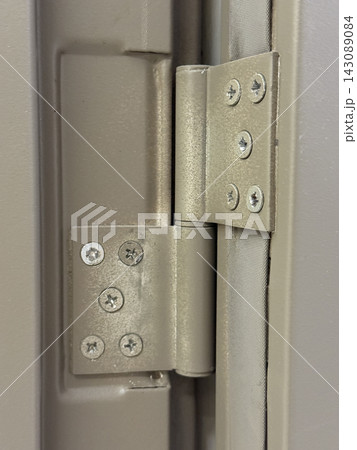 Close-up of metal door hinges with visible screws mounted between painted frame and door edge Close-up of metal door hinges with visible screws mounted between painted frame and door edge 143089084