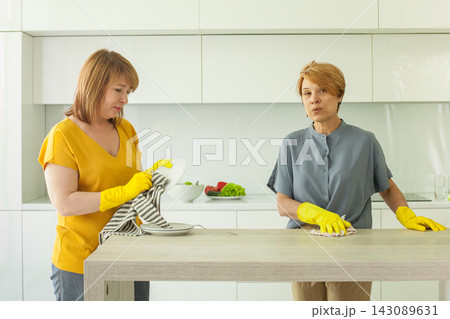 Housekeeping. Mature women cleaning their modern apartment kitchen together. Housekeeping. Mature women cleaning their modern apartment kitchen together. 143089631
