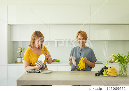 Portrait of mature women cleaning their modern apartment kitchen together. Portrait of mature women cleaning their modern apartment kitchen together. 143089632