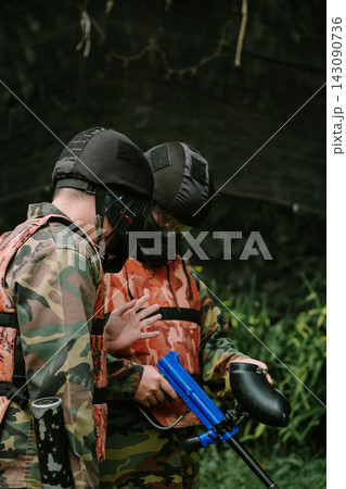 Paintball Players Strategizing Outdoors in Camouflage Gear Paintball Players Strategizing Outdoors in Camouflage Gear 143090736