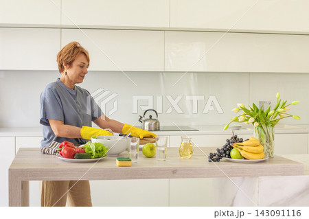 Senior woman wearing yellow rubber gloves wiping in kitchen, indoor portrait 143091116