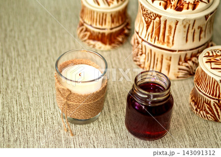 Rustic candle and small glass jar with dark liquid beside carved ceramic containers on table Rustic candle and small glass jar with dark liquid beside carved ceramic containers on table 143091312