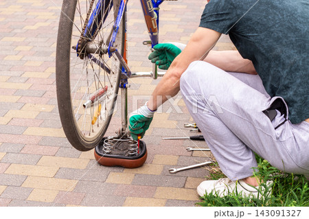 Man examining bike chain and gears for wear. Upside down position reveals issues. Practical competence outside house 143091327