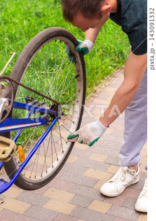 Man fixing bicycle wheel at doorstep. Own vehicle maintenance without service center. Responsible ownership visible. Summer commute switched to pedal power 143091332