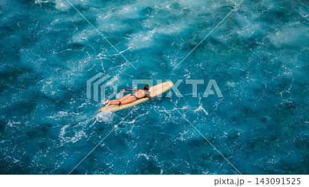 Aerial view of surf girl paddling on longboard through crystal blue ocean water Aerial view of surf girl paddling on longboard through crystal blue ocean water 143091525