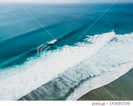Drone view of long surfing waves breaking across a turquoise ocean surface 143091530