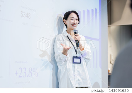 スクリーンのグラフを背景に笑顔でプレゼンテーションする日本人女性 143091620