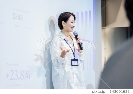 スクリーンのグラフを背景に笑顔でプレゼンテーションする日本人女性 143091622