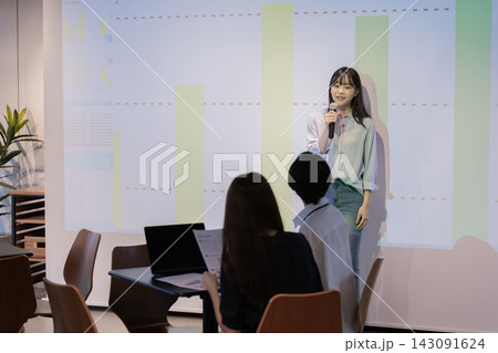 グラフを投影したスクリーンの前でプレゼンテーションする日本人女性 143091624