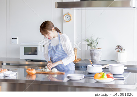 明るいキッチンで玉ねぎを包丁で切るエプロン姿の日本人女性 明るいキッチンで玉ねぎを包丁で切るエプロン姿の日本人女性 143091820