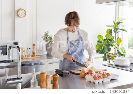 明るいキッチンで玉ねぎを包丁で切りながら料理する若い日本人女性 明るいキッチンで玉ねぎを包丁で切りながら料理する若い日本人女性 143091884