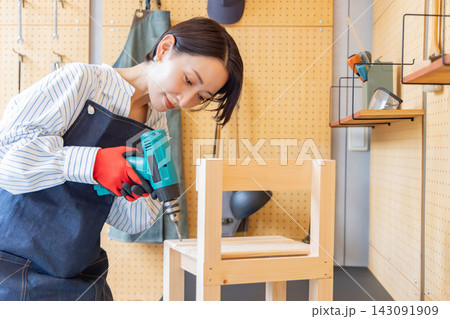 DIY工房で電動ドリルを使い木製椅子を組み立てる日本人女性 DIY工房で電動ドリルを使い木製椅子を組み立てる日本人女性 143091909