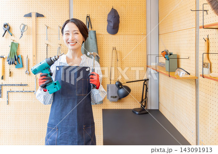 DIY工房で電動ドリルとハンマーを持つ笑顔の日本人女性 DIY工房で電動ドリルとハンマーを持つ笑顔の日本人女性 143091913