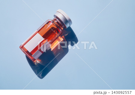 Medical vial containing orange liquid with blank labels reflects on blue surface 143092557