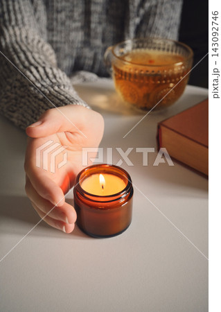 Female hand feeling warmth of candle during quiet evening ritual with tea and book Female hand feeling warmth of candle during quiet evening ritual with tea and book 143092746