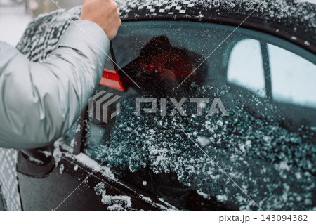 Man scraping ice and snow from car side window with red scraper Man scraping ice and snow from car side window with red scraper 143094382